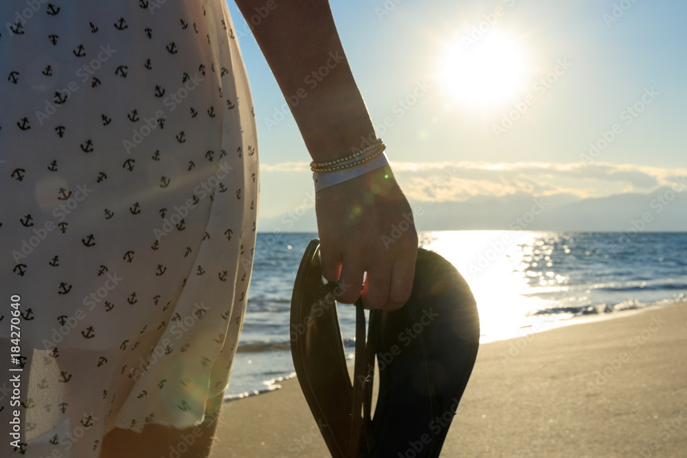 Junge, sexy Frau läuft flaniert am Strand Meer entlang. In der Hand hält  sie Flip Flops. Träumend Selfie mit Handy, Welliges Meer und oranger  Sonnenuntergang in den Bergen Stock-Foto | Adobe Stock