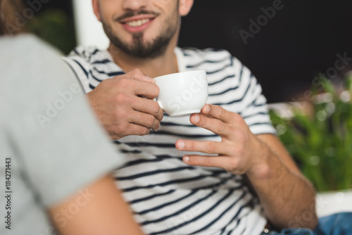 cropped shot of smiling young man drinking coffee on date with girlfriend