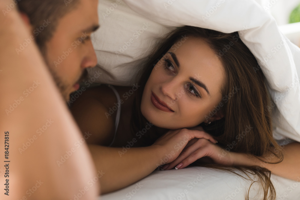 young couple under blanket looking at each other in bed young couple under blanket looking at each other in bed
