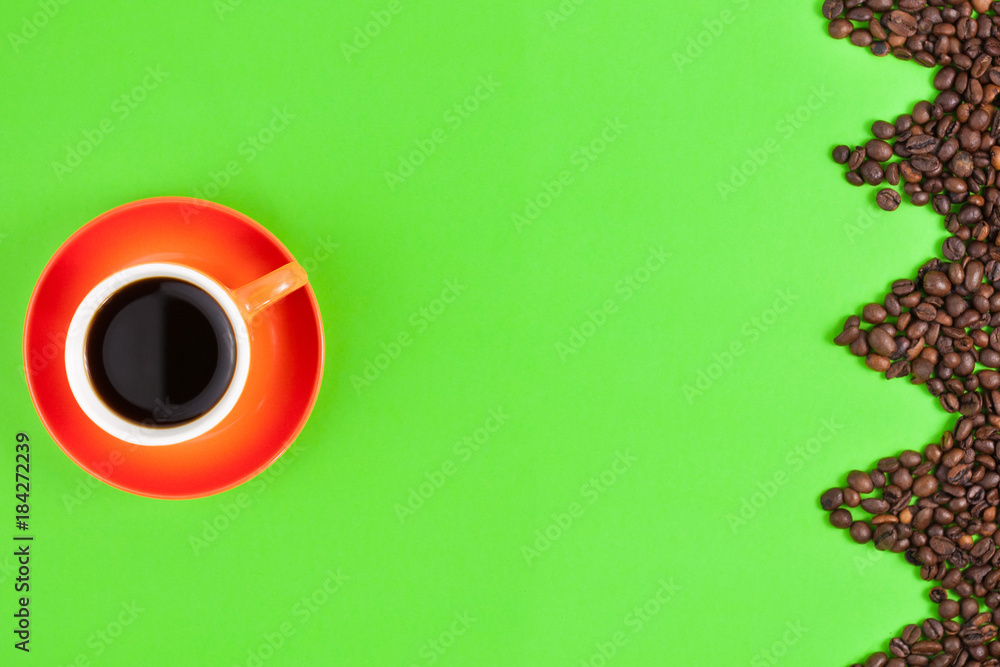Lot of roasted coffee beans laid out in form zigzag on green paper beside full ceramic cup of black coffee on orange saucer Lot of roasted coffee beans laid out in form zigzag on green paper beside full ceramic cup of black coffee on orange saucer