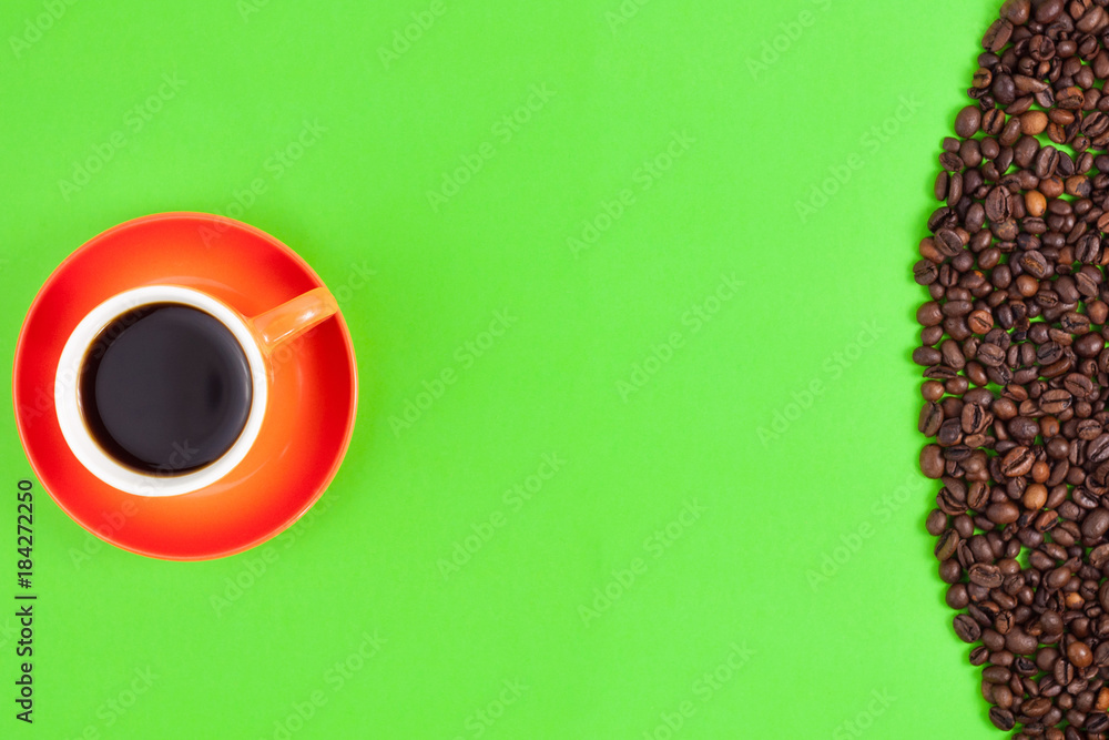 Lot of roasted coffee beans scattered on green paper beside full ceramic cup of black coffee on orange saucer