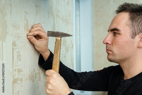A man hammers a nail into plaster wall under the Wallpaper photo