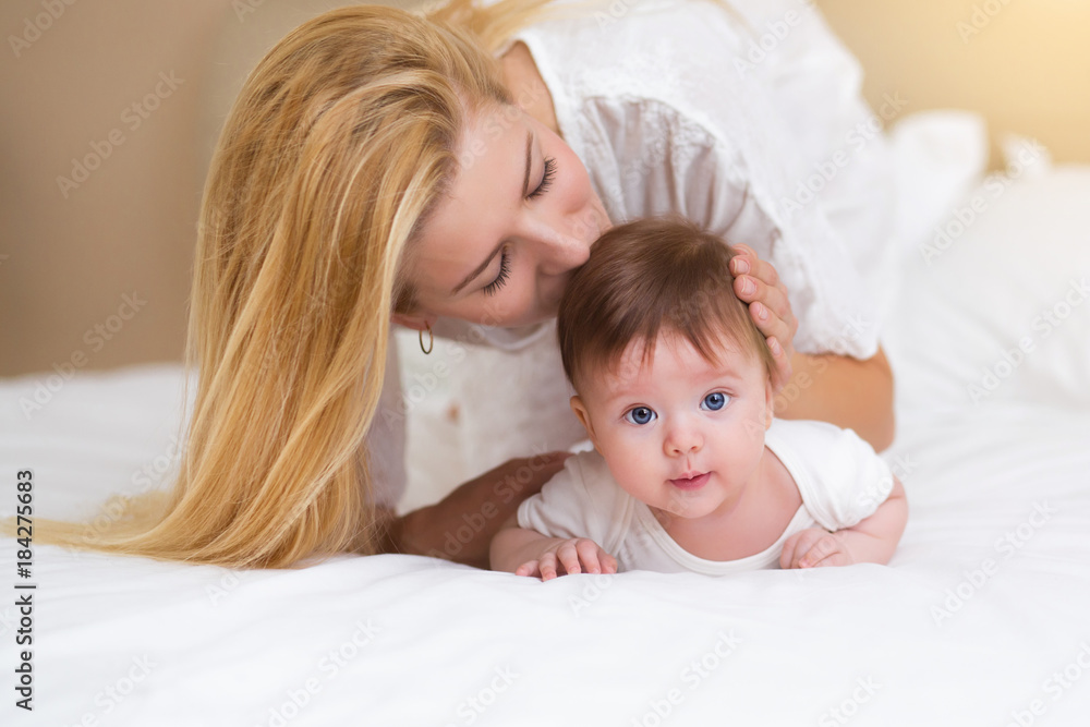Happy loving family concept. Beautiful mother playing with her baby girl in the bedroom. They smiling and hugging together on white bed linens Happy loving family concept. Beautiful mother playing with her baby girl in the bedroom. They smiling and hugging together on white bed linens