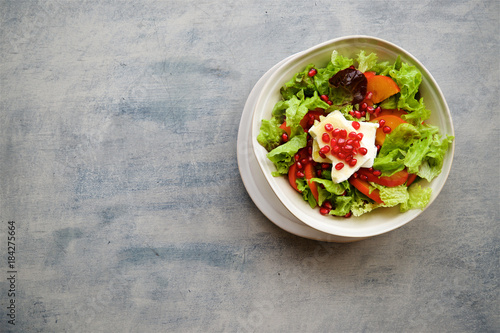 Seasonal salad with persimmon, pomegranate and dressing from honey and mustard. Wooden background, top view
