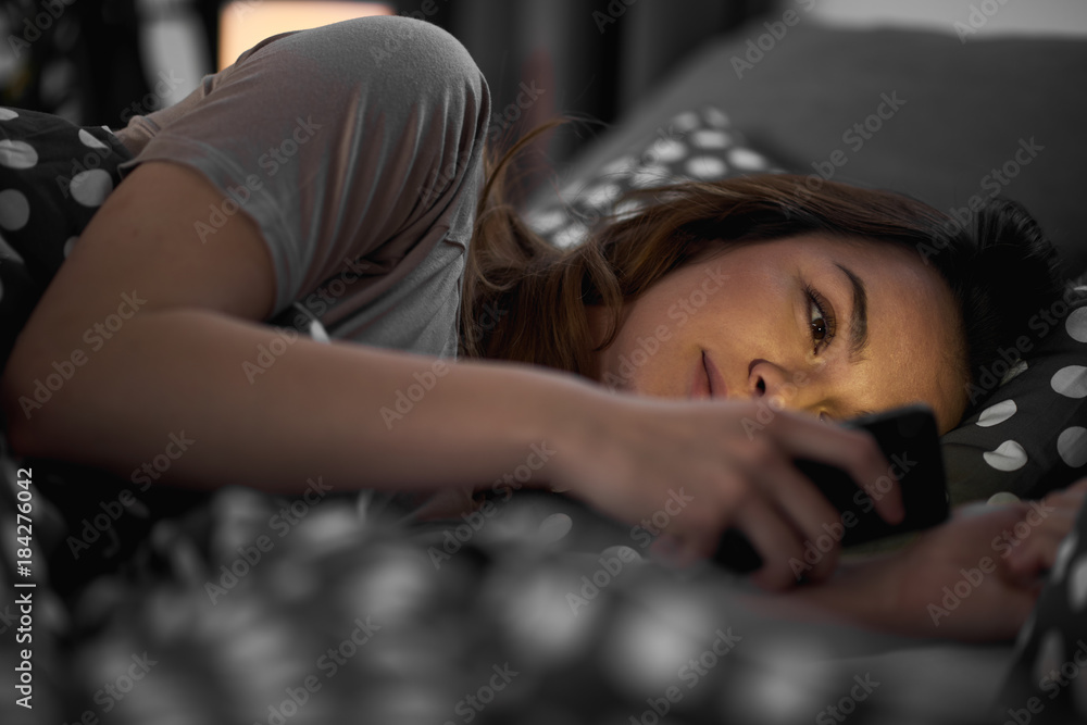 Girl using smart phone and lying down in bed late at night