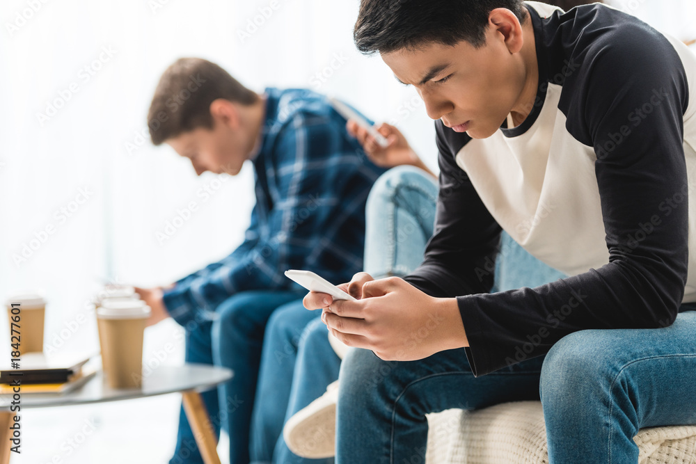 three serious teenagers sitting with smartphones three serious teenagers sitting with smartphones