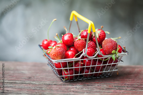 Summer harvest fresh fruits cherries strawberries in shopping basket. Shallow depth field, selective focus, wooden background
