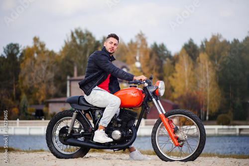 large portrait of a young sporty fashionable man on a motorcycle, a warm shot, late autumn