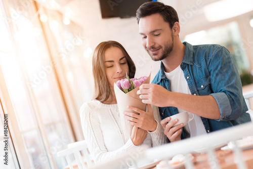 The guy gives flowers to the girl in the cafe.