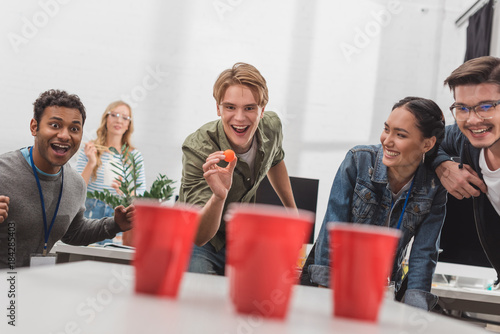 Canvas Print young attractive people playing beer pong at modern office after work