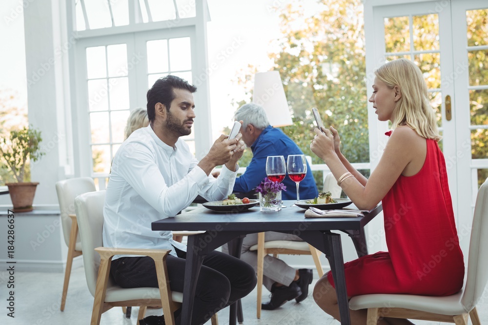 Couple using mobile phone while having meal