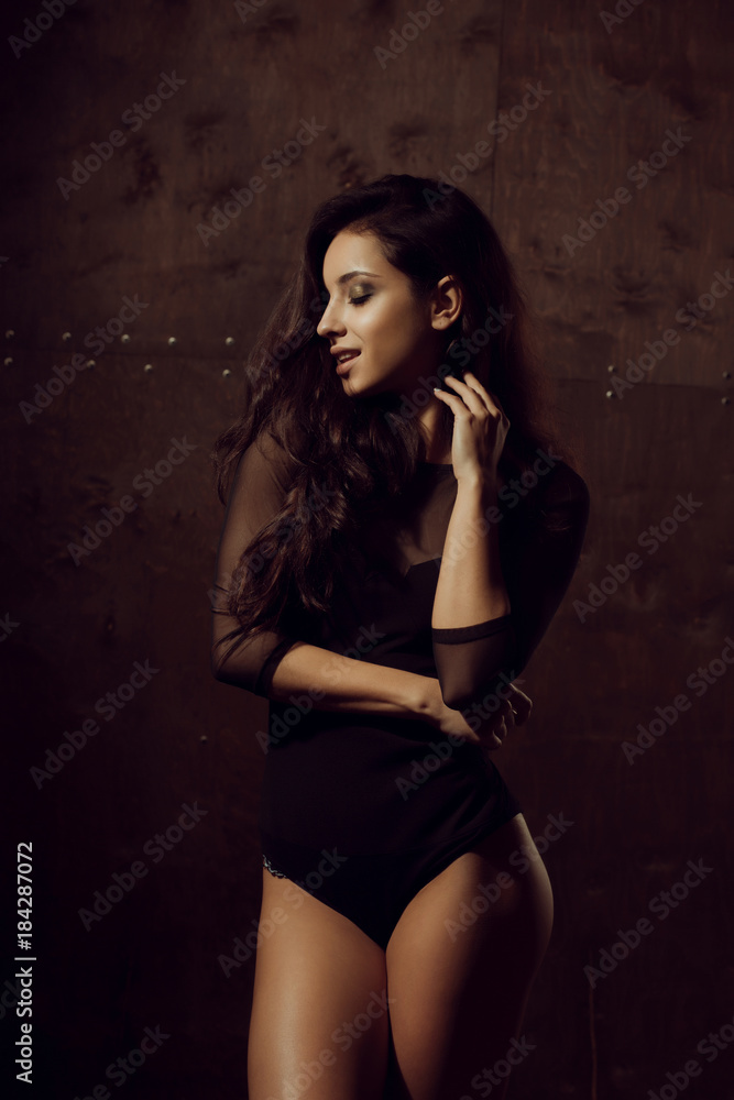 Seductive brunette woman with athletic body and long hair posing in black underwear. Shadow and light