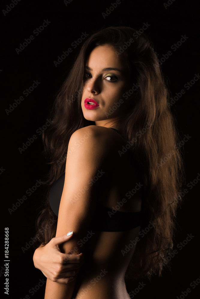 Seductive tanned woman with bright makeup and long hair posing in black bra. Shadow and light