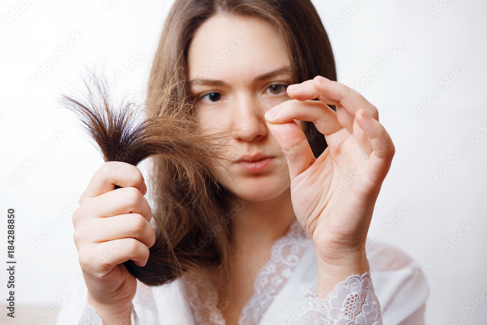 Fototapeta premium girl looks at damaged hair tips, split hair, girl looks at her hair