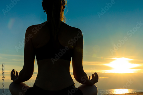 Young sexy woman is doing her yoga workout exercises at a beautiful beach sunset. looking at the ocean landscape. sundown