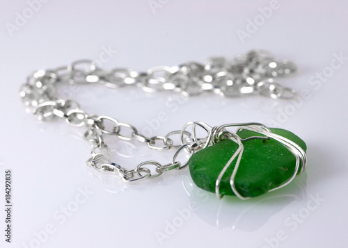 Sea glass necklace with silver chain on white reflective surface. photo