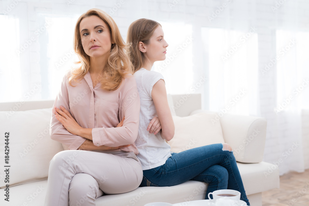 A woman and a girl are sitting on the sofa back to back.