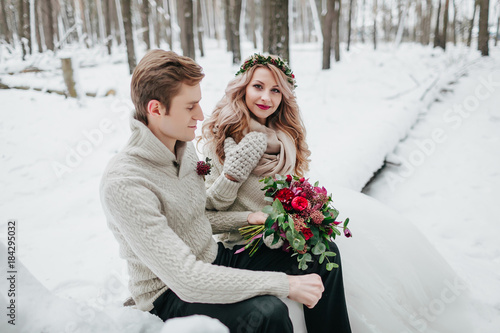 Beautiful bride and groom posing on background of snowy forest. Selective focus on the bride photo