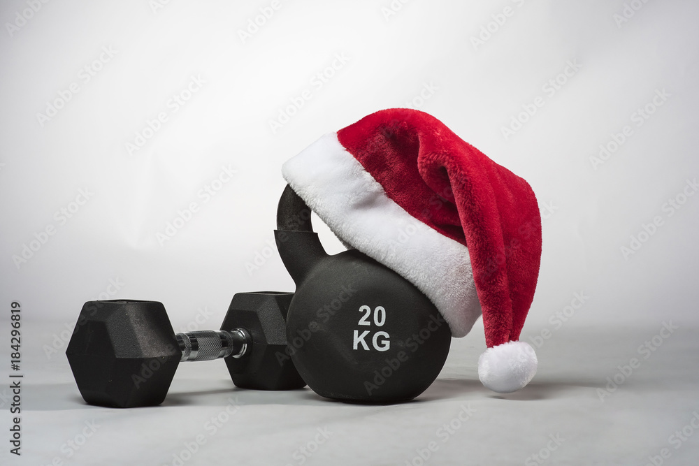 A large black Kettlebell wearing a red Santa hat with a dumbbell next