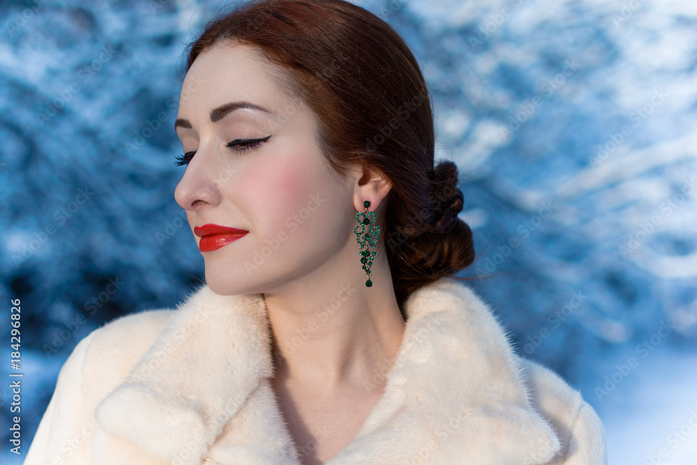 Luxurious woman in a white mink coat and earrings with emerald. Magnificent vintage makeup. Lady of the aristocratic look in the winter Luxurious woman in a white mink coat and earrings with emerald. Magnificent vintage makeup. Lady of the aristocratic look in the winter