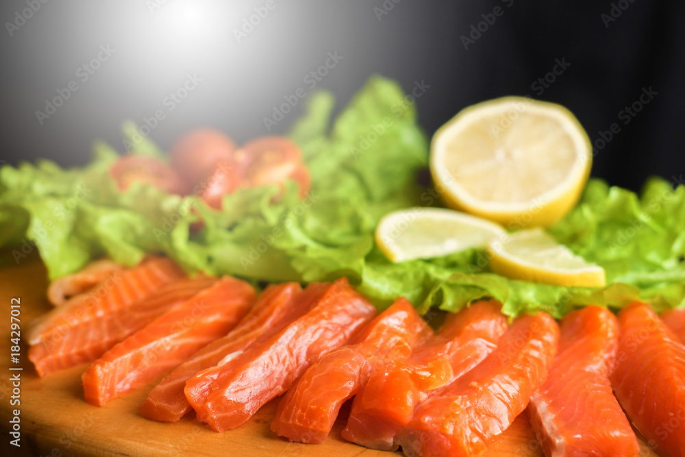 pieces of red fish with lemon and cherry tomatoes on a wooden board on a black background pieces of red fish with lemon and cherry tomatoes on a wooden board on a black background