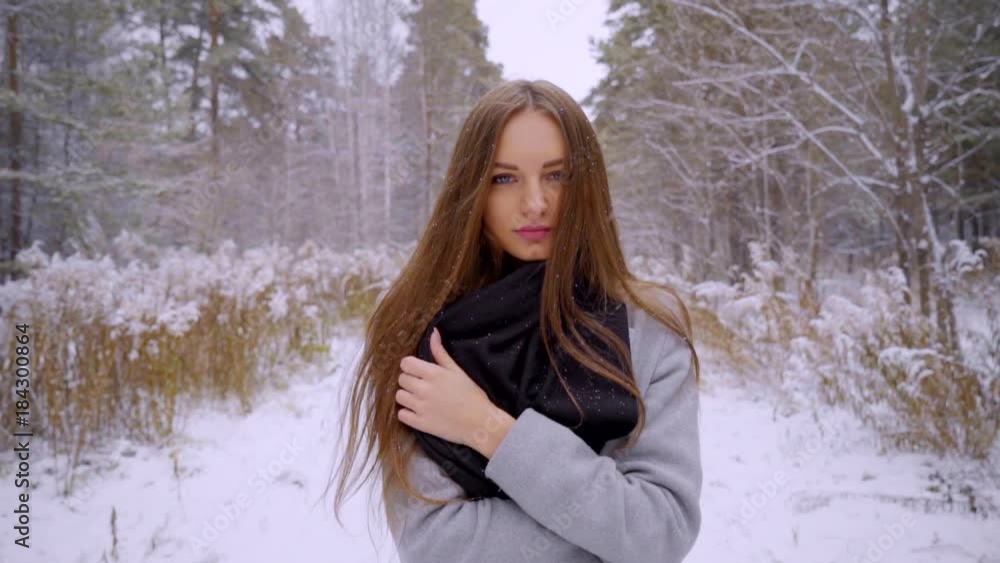 Close up Portrait of stylish young beautiful woman walking outdoors in a winter park over snowy background. looking to the camera. It is snowing. beautiful young woman is walking in a winter park Close up Portrait of stylish young beautiful woman walking outdoors in a winter park over snowy background. looking to the camera. It is snowing. beautiful young woman is walking in a winter park