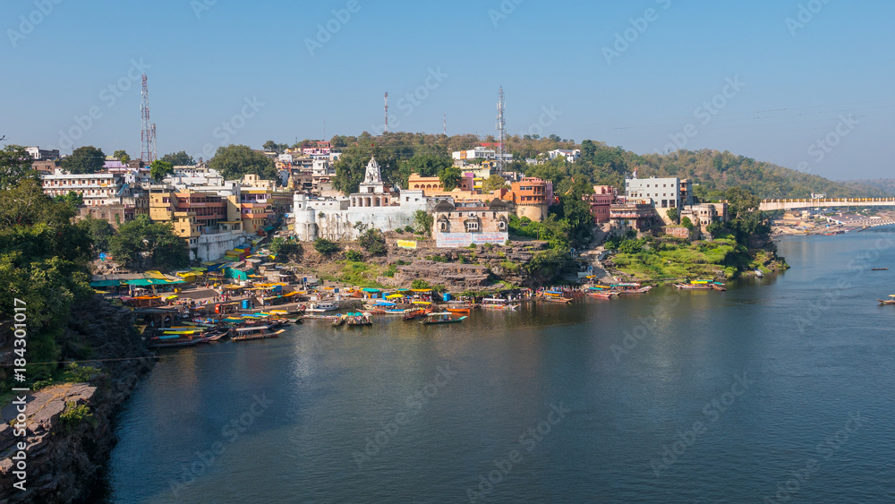 Omkareshwar cityscape, India, sacred hindu temple. Holy Narmada River, boats floating. Travel destination for tourists and pilgrims.
