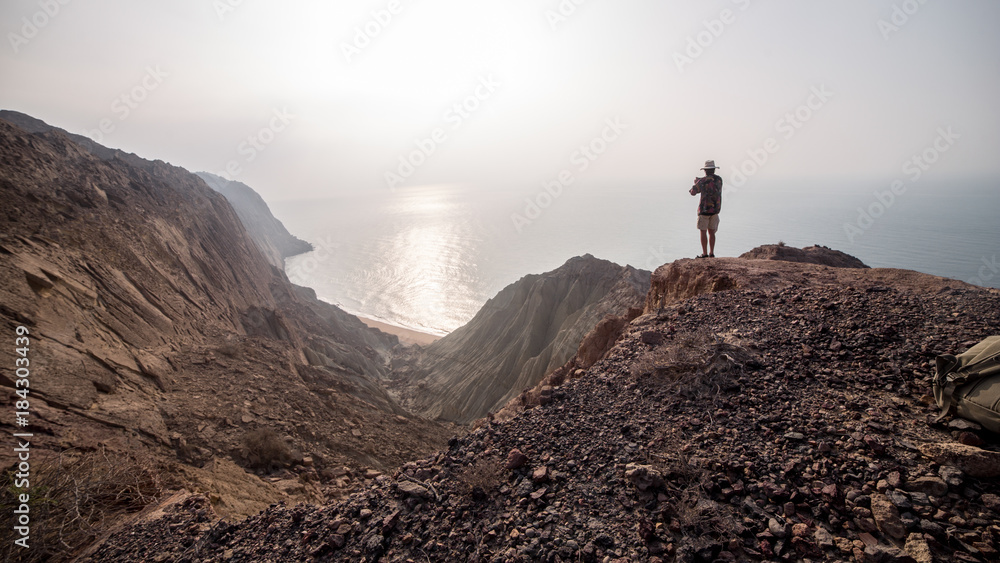 A man taking picture on the top of the desert mountains near the sea