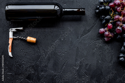 Uncorking the wine bottle. Bottle, corkscrew and bunches of red and black grapes on black background top view copyspace
