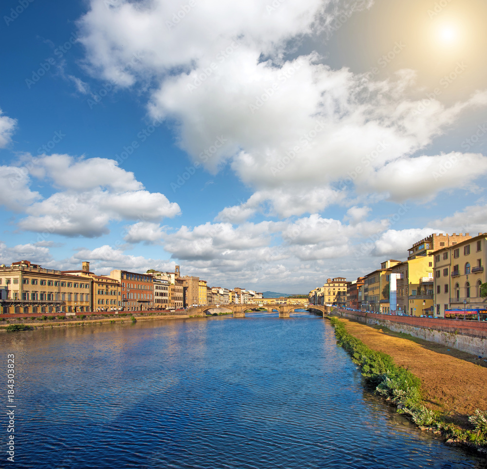 Fototapeta premium Beautiful city view with the famous medieval stone bridge Ponte Vecchio over the Arno river in Florence, Italy at sunny day. Place of pilgrimage for tourists.