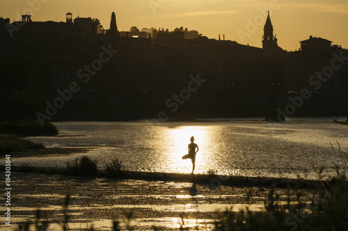 Young Japanese woman practicing yoga exercises near a river in a summer day in the city at sunset
