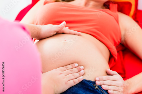 Midwife exanimating belly of lying pregnant woman manually with both hands photo