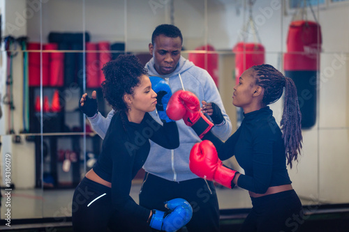 Experienced boxing trainer supervising and teaching two female boxers indoors