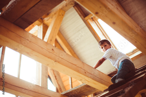 Charming little child sits on the wooden ladder under the roof