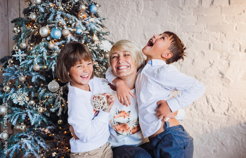 Charming blonde mother hugs her children tender posing before a Christmas tree