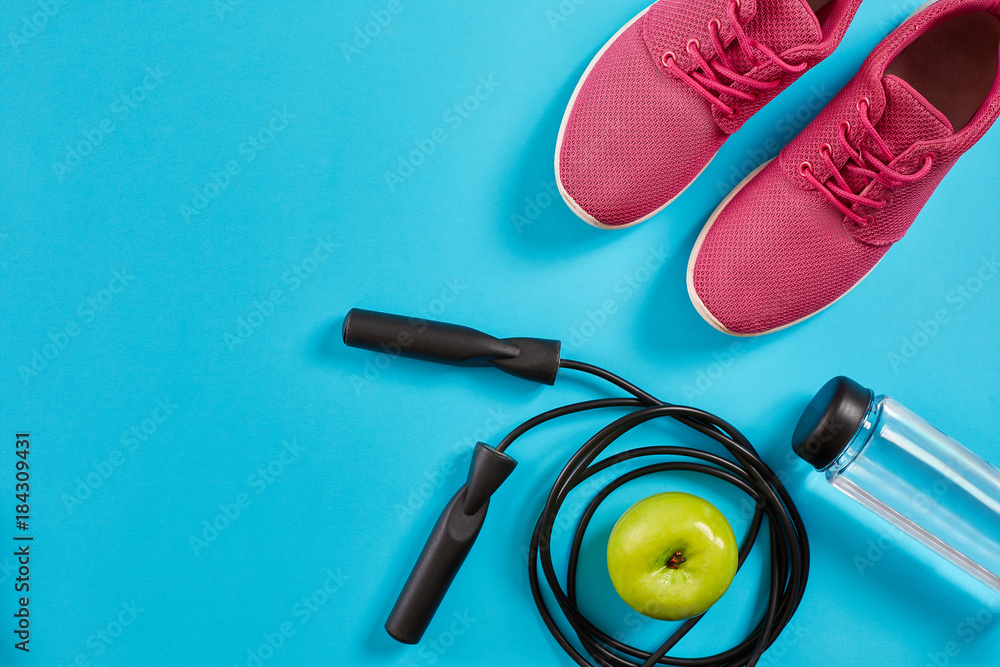 Flat lay of female sport equipments, jump rope, bottle of water and pink sneakers on blue background