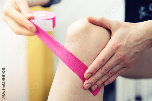 woman taping her knee with kinesio tape