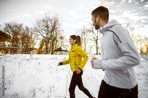Active fitness sportive couple jogging with earphones on the snow covered road in nature in the morning. © dusanpetkovic1
