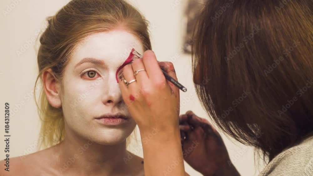 Face art. Makeup artist drawing red lines on the model's face. Face art. Makeup artist drawing red lines on the model's face.