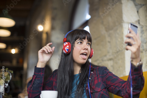 Fotografie Ragazza con cuffie ascolta la musica dal suo cellulare seduta in un locale