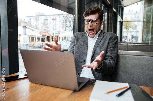 Angry shocked business man in eyeglasses sitting by the table