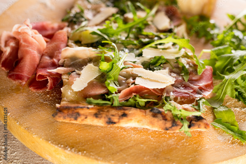 Pizza with Parma ham and cheese shavings on bed of rocket salad