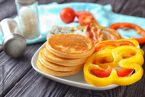 Plate with yummy pancakes and bacon on wooden table