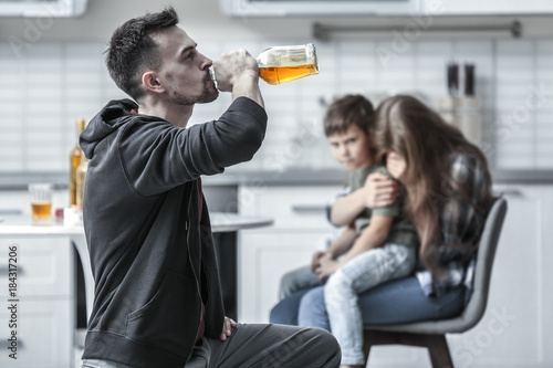 Man drinking alcohol while wife hugging their son on background photo