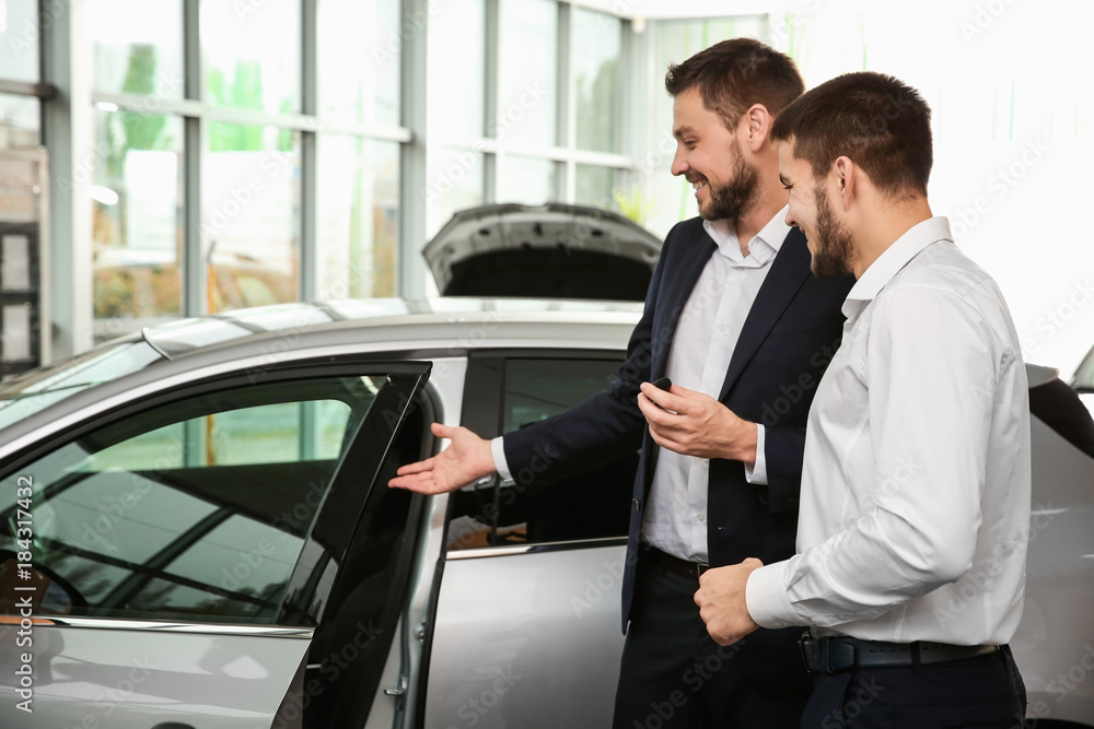 Handsome car salesman with trainee looking at automobile in dealership centre Handsome car salesman with trainee looking at automobile in dealership centre