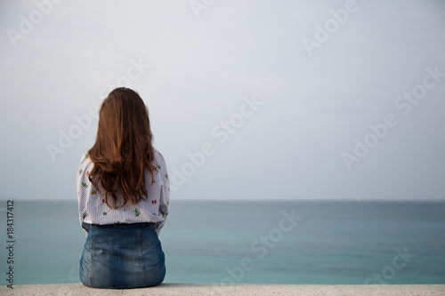 Photos Young woman sitting and looking out to the sea. Rear back view.