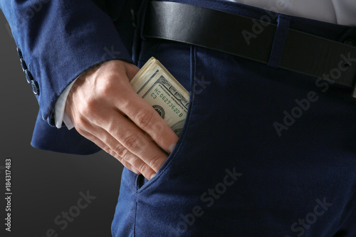 Man in formal suit putting money in pocket on dark background, closeup