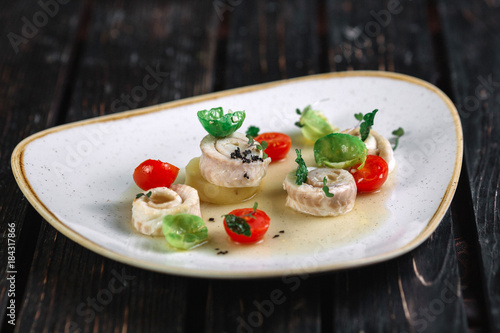 Rolled herring with vegetable on irregular shape plate on dark wood background