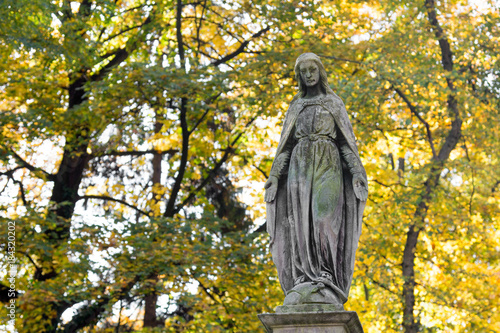 Statue of Mary Mother of God, at autumn tree backgroung, copy space. Religious symbol.