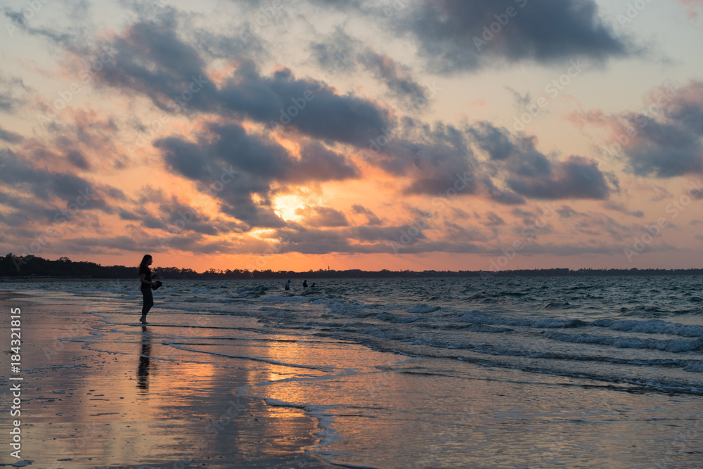 Einzelne Frau beim Spaziergang am Strand während Sonnenuntergang blickt aufs Meer